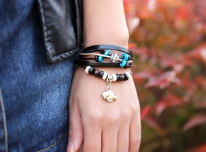Detail of layered leather bead bracelet with silver fish charm worn on wrist outdoors