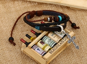 Close-up of multilayer leather bracelet featuring a vintage silver crucifix and wooden beads