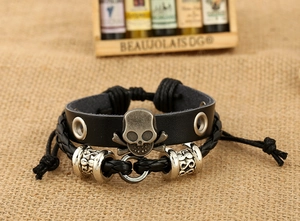 Détail d'un bracelet punk en cuir avec crâne en bronze et cordon tressé sur fond de toile de jute