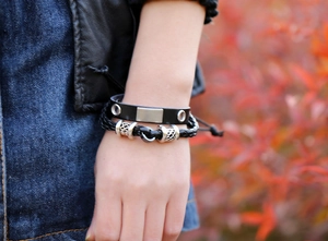 Close-up of a men's black leather bracelet set with metallic beads and engraved accents