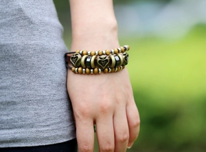 Dettaglio di un bracciale vintage multistrato in pelle con perline in legno e cuore di bronzo
