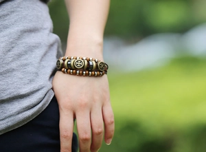 Detail of multi-layer beaded leather bracelet with cross charm on a wrist in nature