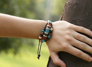 Detail of bohemian leather bracelet with blue crystal beads worn against a forest background