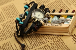 Detail of vintage multilayer leather bracelet watch featuring beads and feather charm