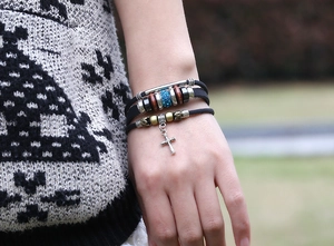 Detail of bohemian layered leather bracelet with silver cross and wooden beads