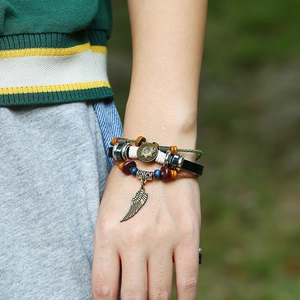 Detail of bohemian layered leather bracelet featuring bronze feather charm and wooden beads