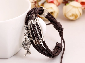 Macro detail of braided brown leather bracelet with silver wing charm and vintage metal beads
