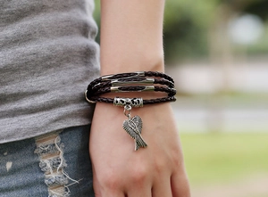 Detail of vintage braided leather bracelet with silver metal tubes and angel wing charm