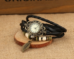 Macro detail of retro quartz watch with braided leather strap and bronze leaf charm