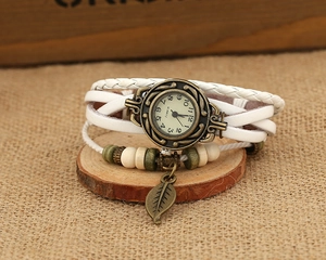 Macro view of white leather wrap watch with bronze leaf charm and vintage quartz dial