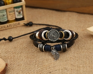 Dettaglio di bracciale in pelle multistrato con piuma e ciondoli in metallo su juta