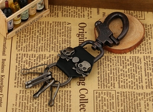 Close-up of bronze carabiner keychain with black leather and dual metal skulls detail