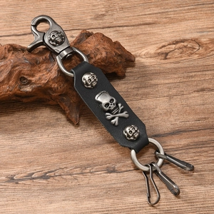 Detail of punk leather keychain with silver skull charms and spring snap hook on wood