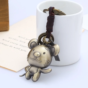 Vintage bronze rat zodiac keychain with leather strap on a decorative white cup