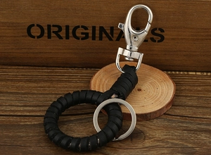 Detail of a handmade black leather braided keychain with silver lobster clasp on wood
