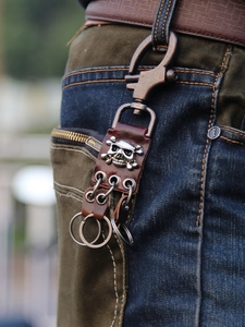 Retro brown leather keychain with metal skull design hanging on denim jeans