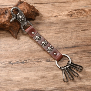 Close-up of vintage leather skull keychain with metal hooks on rustic wood background