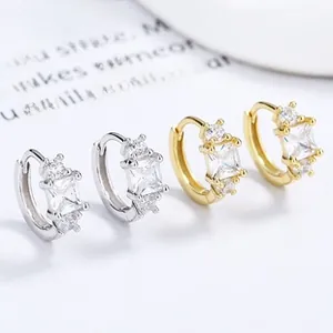 Detail of square zircon earrings in silver and gold plating on a minimalist white card