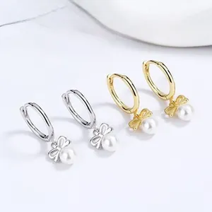 Macro view of 925 silver and gold earrings featuring bow details and lustrous white pearls