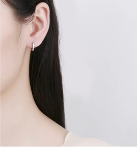 Gros plan d'une créole minimaliste en argent 925 avec zircons pavés sur l'oreille du mannequin