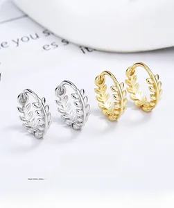 Détail macro de boucles d'oreilles créoles feuilles en argent 925 et or sur fond blanc