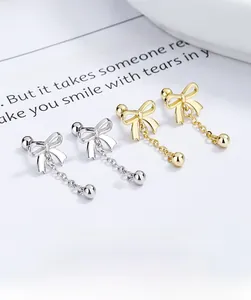 Detailed view of silver and gold bow tassel stud earrings on a minimalist background