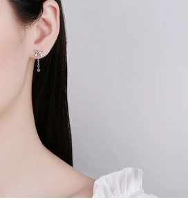 Close-up of 925 sterling silver bow tassel earrings worn by a model in soft lighting