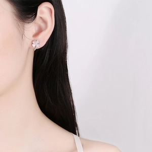 Sterling silver four-leaf clover stud earrings with pink petals on a model's ear