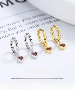 Detail of 925 silver and 18K gold heart earrings with red gemstones and beaded hoops