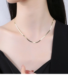 Detailed close-up of a delicate gold flat snake chain necklace on a model's collarbone