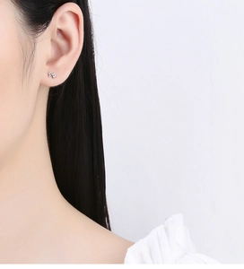 Detailed view of silver bow-shaped stud earring worn on earlobe for a minimalist look