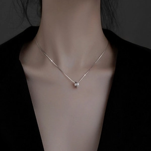 Macro shot of silver cylindrical pendant on a minimalist chain worn by a female model
