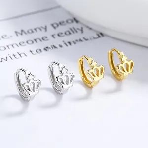 Close-up of small crown hoop earrings in gold and silver finishes on a magazine background