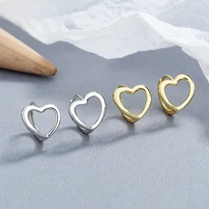 Macro detail of gold and silver heart hoop earrings on minimalist textured background