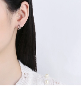 On-ear view of sterling silver hollow heart earrings with polished finish on model