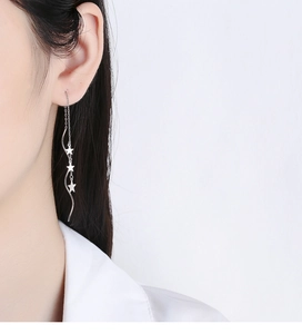 Detail of 925 sterling silver star tassel earrings with long wave chain on model ear