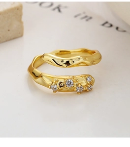 Close-up of golden irregular wavy ring with sparkling zircons on a textured surface