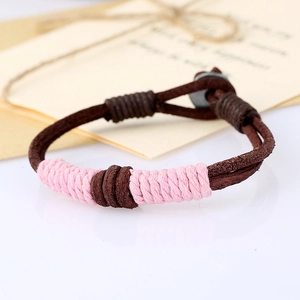 Close-up of woven brown leather bracelet with pink cord accents and disc button closure