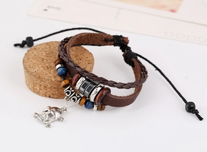 Macro detail of multi-layer leather bracelet with silver skull charm and wooden beads