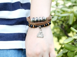 Nahaufnahme eines mehrlagigen Lederarmbands mit Buddha-Anhänger und Perlen am Handgelenk