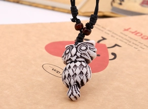 Detail of owl pendant necklace with intricate carvings and dark wood beads on woven cord