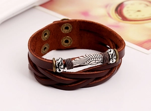 Detail of vintage braided leather bracelet featuring a silver wing charm and bronze buckle