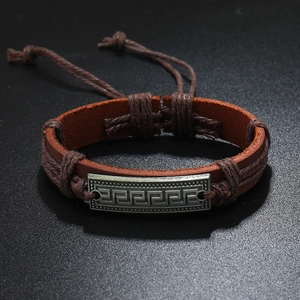 Detail of vintage brown braided leather bracelet with engraved Greek meander metal plate