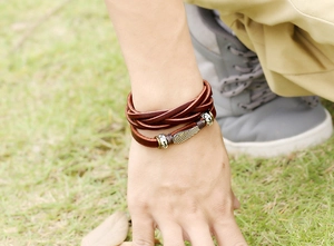 Detail of multi-layer leather bracelet with silver feather pendant on a wrist outdoors