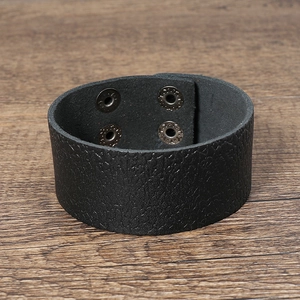 Détail d'un bracelet manchette en cuir noir texturé avec boutons-pression en argent