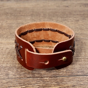 Handmade vintage wide brown leather bracelet with woven details on a wooden background