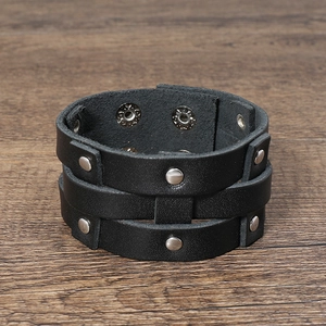 Detail of black multi-layer leather bracelet featuring silver metal studs on wood texture
