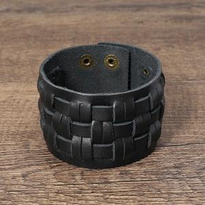 Detail of multi-layer woven black leather bracelet with bronze snap buttons on wood