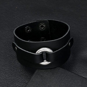 Detail of a black wide leather cuff bracelet featuring a silver metal ring and snap fasteners