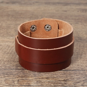 Detail of dark brown leather bracelet with silver metal snap buttons on wood background